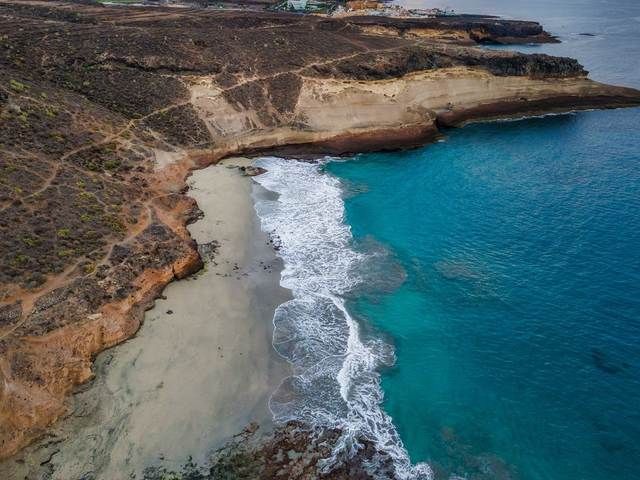Una cala de arena aislada entre acantilados ocres en la costa de Tenerife